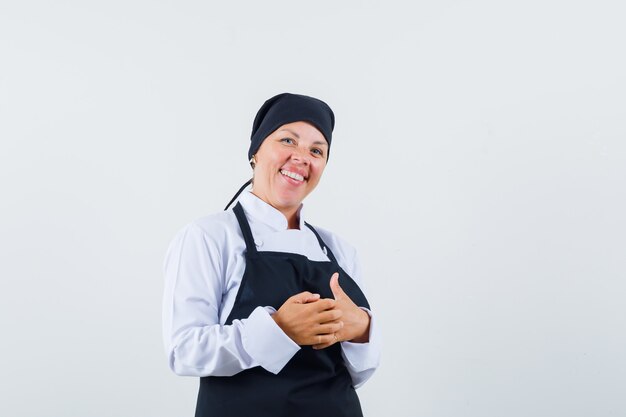 Blondevrouw die handen in zwarte uniforme kok wrijven en op zoek mooi, vooraanzicht.