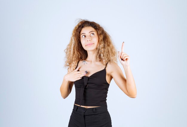 Blondiemeisje steekt haar hand op en wijst iets boven met emoties.