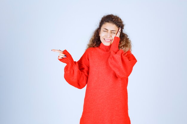 Blondievrouw in rood sweatshirt die ergens aan de linkerkant wijst.