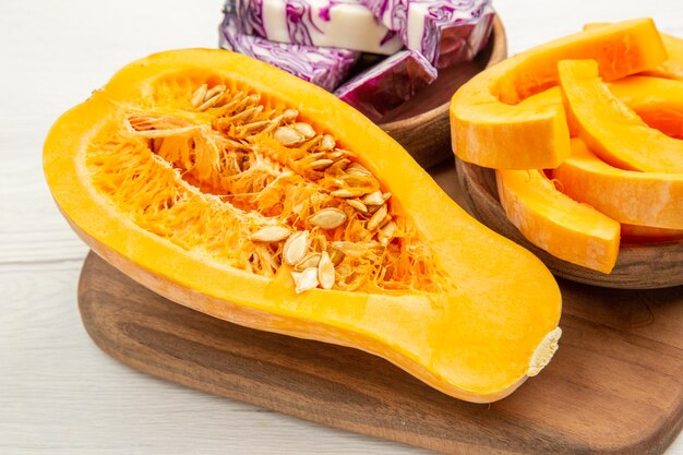 Bodem van dichtbij bekijken butternut squash in tweeën gesneden rode kool en squash plakjes in kommen op snijplank op witte tafel