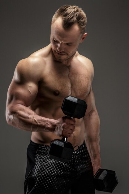 Bodybuilder in zwarte korte broek met dumbell. Studioshoot op grijze achtergrond
