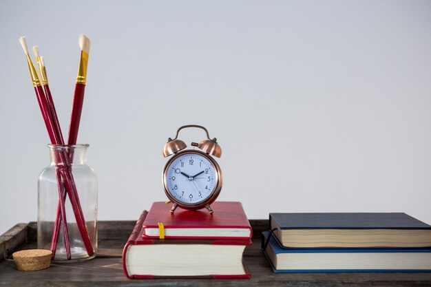 Boeken, wekker en kwast gerangschikt op houten tafel