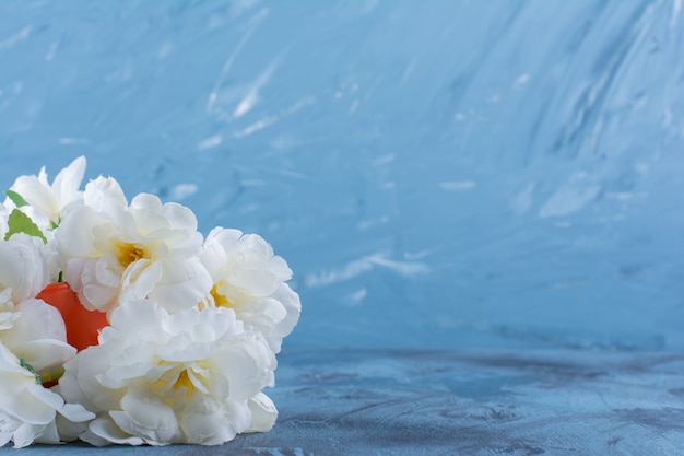 Boeket van bleke bloemen in een oranje vaas op blauw.