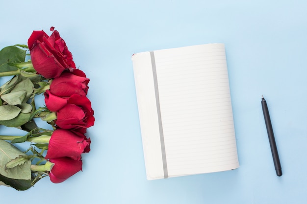 Gratis foto boeket van rode bloemen dichtbij notitieboekje en pen