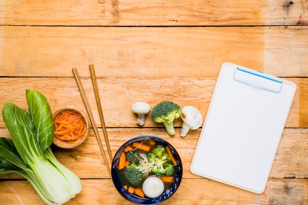 Gratis foto bokchoy; wortel; visbal soep; eetstokjes en witte lege klembord over de tafel