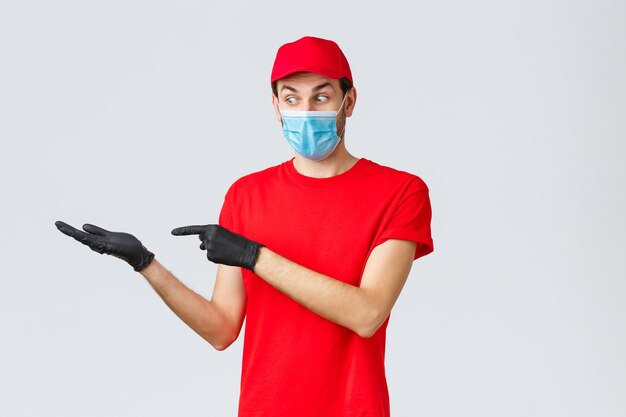 Boodschappen en pakketten bezorgen, covid-19, quarantaine en winkelconcept. Opgewonden en geïntrigeerde koerier in gezichtsmasker en handschoenen introduceren korting of promo op pakketbezorging, houd banner in de hand