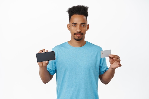 Boos Afro-Amerikaanse man met horizontale smartphone scherm creditcard teleurgesteld met bank-app geen geld bankrekening staan ontevreden tegen witte achtergrond