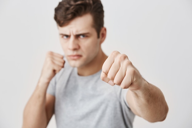 Boos agressief jong Kaukasisch mannetje dat in defensieve positie staat, gebalde vuisten heeft, zelfverzekerde blik heeft, klaar om zichzelf te verdedigen en opkomt voor zijn rechten