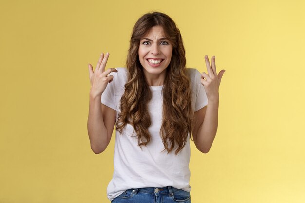 Boos boos boze vrouw gebaren intens handen schudden woedend woedend zijn tanden op elkaar klemmen fronsen grimassen teleurgesteld klagen vloeken vloeken onbeleefd gele achtergrond