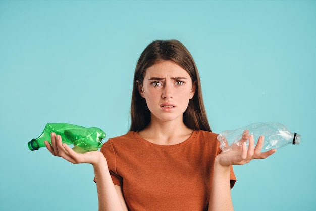 Gratis foto boos casual meisje dat lege plastic flessen in handen houdt terwijl ze helaas naar de camera kijkt over een kleurrijke achtergrond