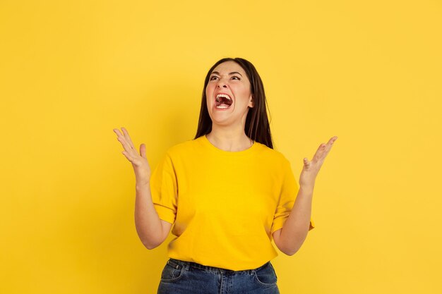 Boos geschreeuw. Blanke vrouw portret geïsoleerd op gele muur. Mooi vrouwelijk donkerbruin model in informele stijl. Concept van menselijke emoties, gezichtsuitdrukking, verkoop, advertentie, copyspace.