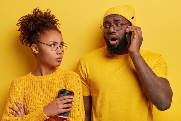 Boos jaloerse Afro-vrouw kijkt naar man die op mobiele telefoon praat