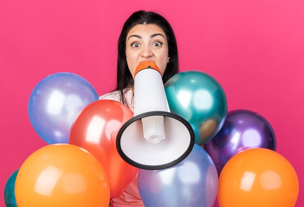 Boos jong mooi meisje dat achter ballonnen staat, spreekt op luidspreker