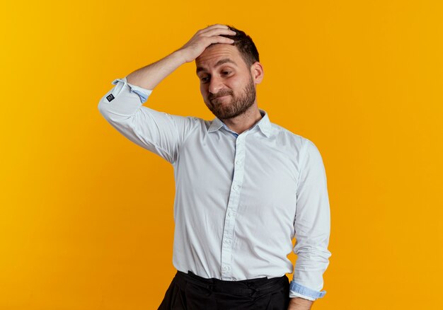 Boos knappe man legt hand op voorhoofd neerkijkt geïsoleerd op oranje muur