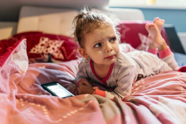 Boos meisje met smartphone liggend op bed