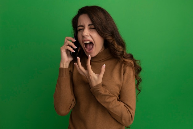 Boos met gesloten ogen jong mooi meisje spreekt over telefoon geïsoleerd op groene muur