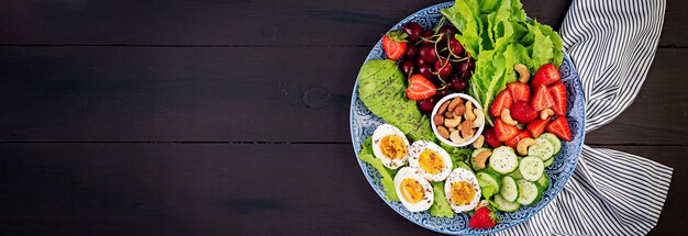 Bord met een paleo dieetvoeding. Gekookte eieren, avocado, komkommer, noten, kersen en aardbeien. Paleo ontbijt. Bovenaanzicht