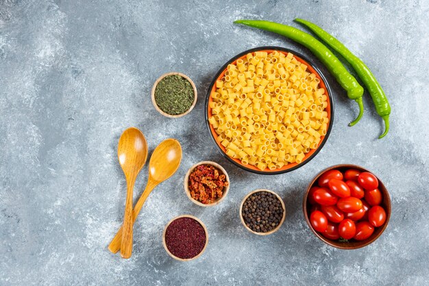 Bord pasta, kom tomaten en kruiden op marmeren achtergrond.