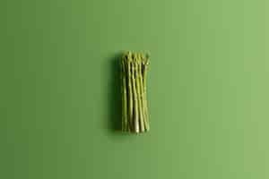 Gratis foto bos van verse asperges op levendige groene achtergrond. ingrediënt voor het bereiden van heerlijke vegetarische salade. voedsel concept. verse lentegroenten. eetbare spruiten van asperges rijk aan vitamines, foliumzuur