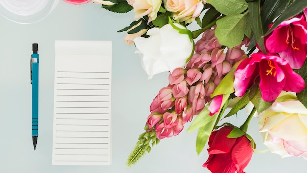 Bos van verse bloemen met pen en blocnote op bureau