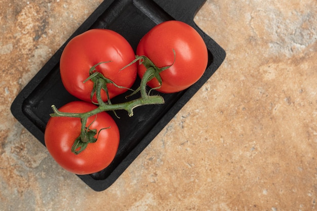 Bos van verse, rode tomaten met groene stengels op donkere plaat