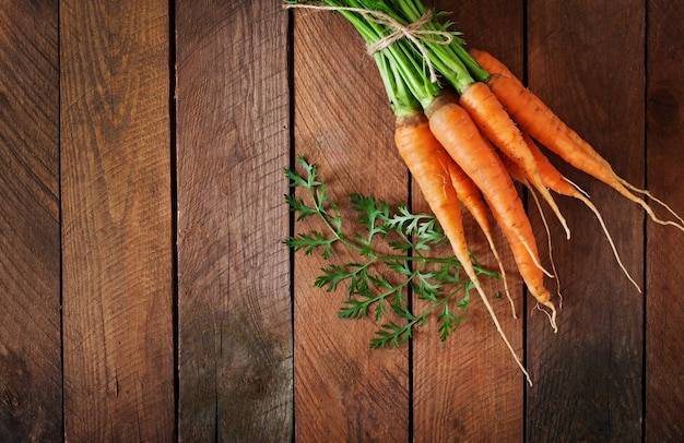 Gratis foto bos van verse wortelen met groene bladeren over houten tafel