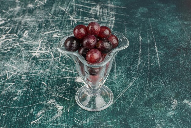 Gratis foto bos van zwarte druiven in glas en op marmeren lijst.