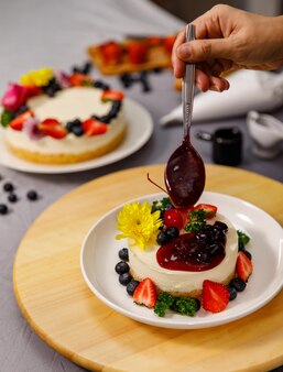 Bosbessensaus gieten op heerlijke zoete cheesecake versierd met verse bessen en bloemen op een houten bord, voor een verjaardag, valentijnsdag en feest