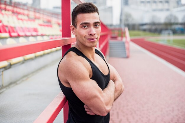 Bouw atleet op met zijn arm gekruist op stadionspoor en veld