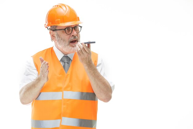 bouwer in een constructie vest en een oranje helm praten op een mobiele telefoon over iets.