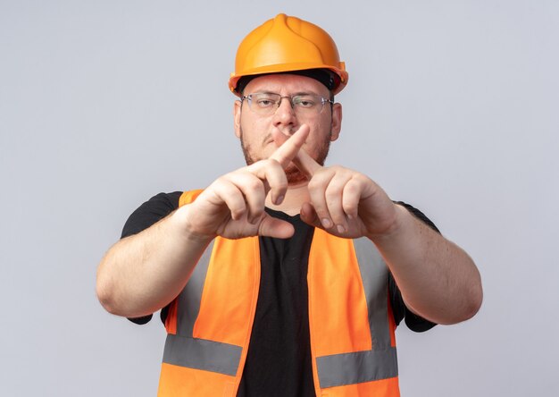 Bouwer man in bouw vest en veiligheidshelm kijken camera met ernstig gezicht defensie gebaar maken van de wijsvingers staande over witte achtergrond