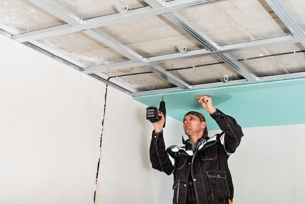 Gratis foto bouwvakker montage verlaagd plafond met gipsplaat en bevestiging van de gipsplaat aan het metalen plafondframe met schroevendraaier.