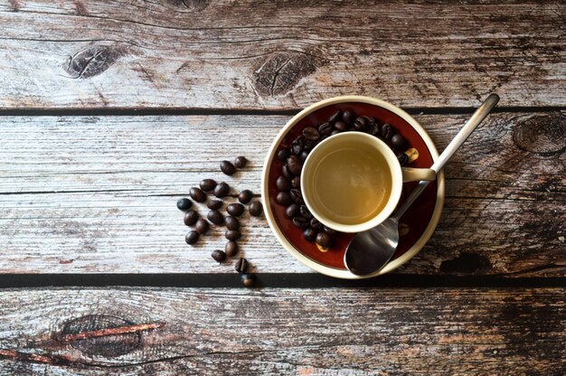 Boven geschoten van een koffiekop dichtbij koffiebonen en een metaallepel op een houten oppervlakte