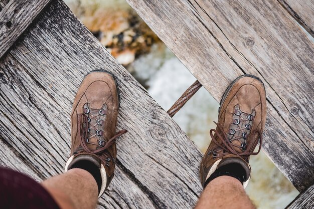 Boven geschoten van mannelijke voeten die zich op een houten brug bevinden die wandelingsschoenen dragen