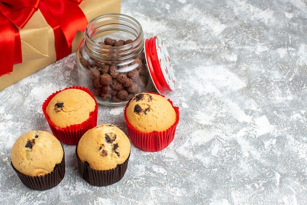 Boven uitzicht op heerlijke kleine cupcakes en chocolade in een glazen pot en dennentakken naast cadeau met rood lint op ijsoppervlak