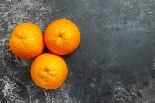 Gratis foto boven weergave van drie natuurlijke biologische verse sinaasappelen aan de rechterkant op donkere achtergrond
