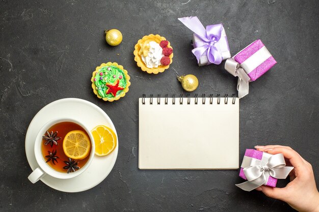 Boven weergave van een kopje zwarte thee met citroen geserveerd met koekjes notbbok en geschenken op donkere achtergrond