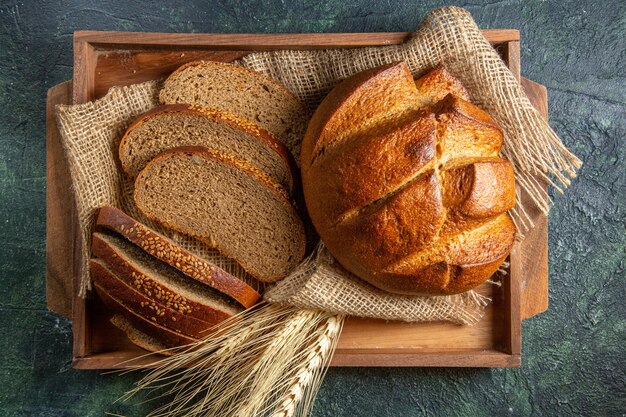 Boven weergave van geheel en vers zwart brood op handdoek in een bruin houten dienblad op donkere mix kleuren oppervlak