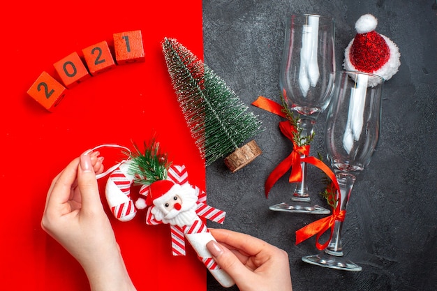 Boven weergave van hand met decoratie accessoires glazen bekers kerstboom nummers kerstman hoed op rode en zwarte achtergrond