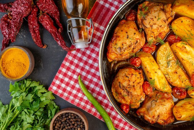 Boven weergave van heerlijk diner met kippen aardappelen Groenen op gevouwen rood gestripte handdoek gedroogde pepers gevallen olie fles gele gember groene bundel aan de rechterkant op donkere kleur achtergrond