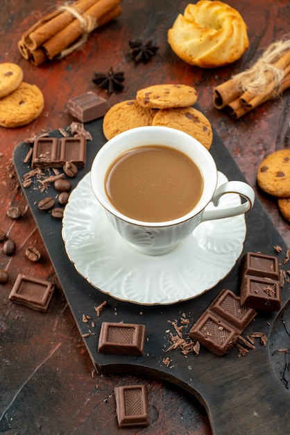 Boven weergave van heerlijke koffie in witte kop op houten snijplank koekjes kaneel limoenen chocoladerepen op gemengde kleur achtergrond