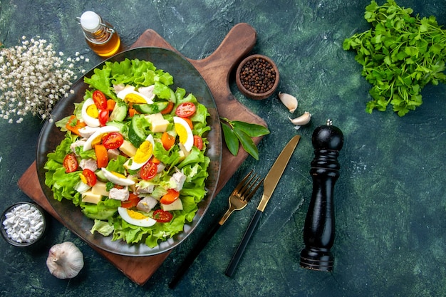 Boven weergave van heerlijke salade met verse ingrediënten op houten snijplank kruiden olie fles knoflook bestek ingesteld op zwarte mix kleuren tafel