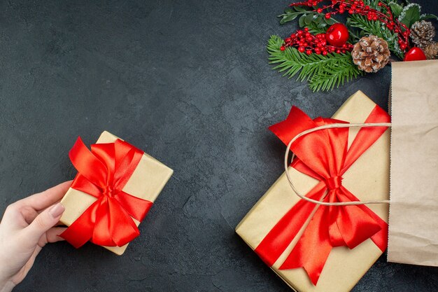 Boven weergave van kerstsfeer met hand met een van de mooie geschenken en fir takken conifer kegel op donkere achtergrond
