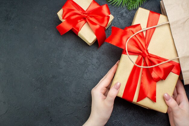 Boven weergave van kerstsfeer met hand met mooie geschenken en fir takken conifer kegel op donkere achtergrond