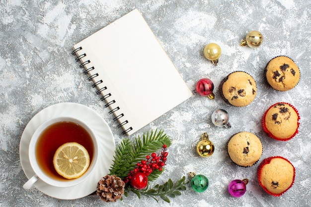 Boven weergave van kleine cupcakes en decoratieaccessoires dennentakken conifer kegel een kopje zwarte thee naast gesloten notitieboekje op ijsoppervlak