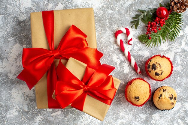 Boven weergave van kleine cupcakes, snoep en dennentakken, decoratieaccessoires en geschenken met rood lint op ijsoppervlak