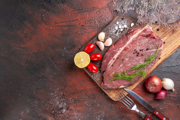 Boven weergave van rood vlees op houten snijplank en knoflook groene citroen ui vork en mes op donkere achtergrond