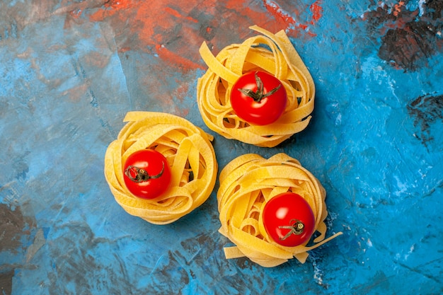 Boven weergave van tomaten op zelfgemaakte pasta's op blauwe achtergrond