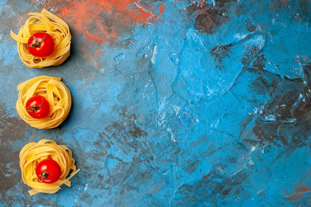 Boven weergave van tomaten op zelfgemaakte pasta's opgesteld in een rij op blauwe achtergrond