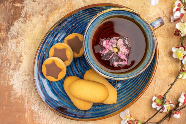 Boven weergave van verschillende koekjes een kopje thee en bloemen op tafel met gemengde kleuren